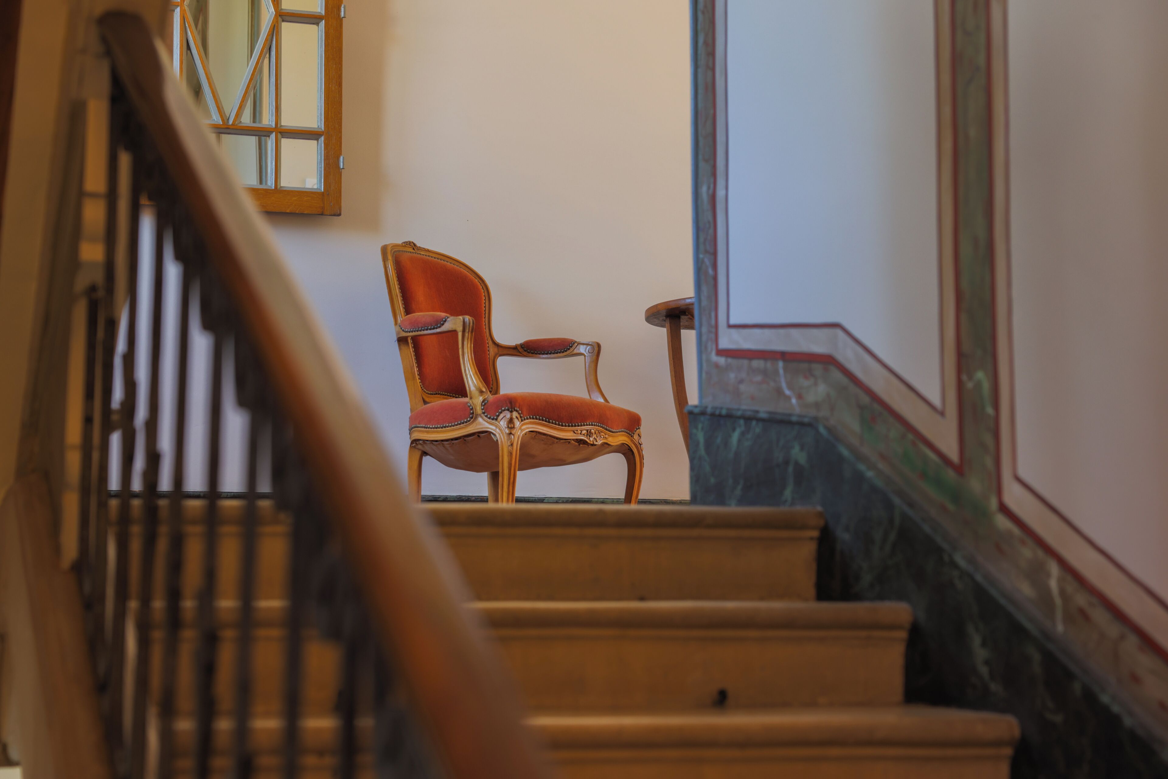 A staircase with a wooden handrail and a red upholstered chair at the top.