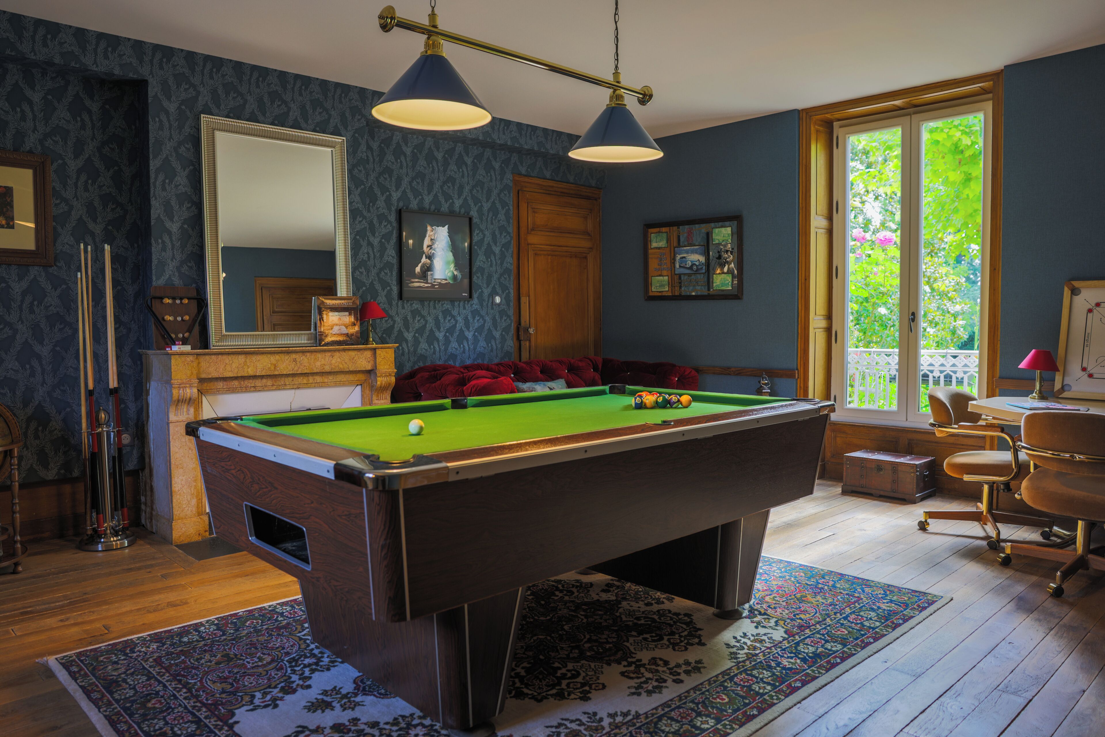 Een pooltafel in een ruimte met een houten vloer, een grote spiegel en een raam met uitzicht op groen.