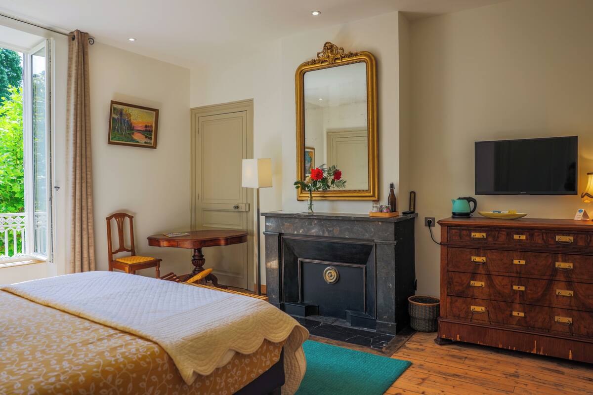 A hotel room with a bed, a fireplace, a dresser, a television, and a window with curtains.