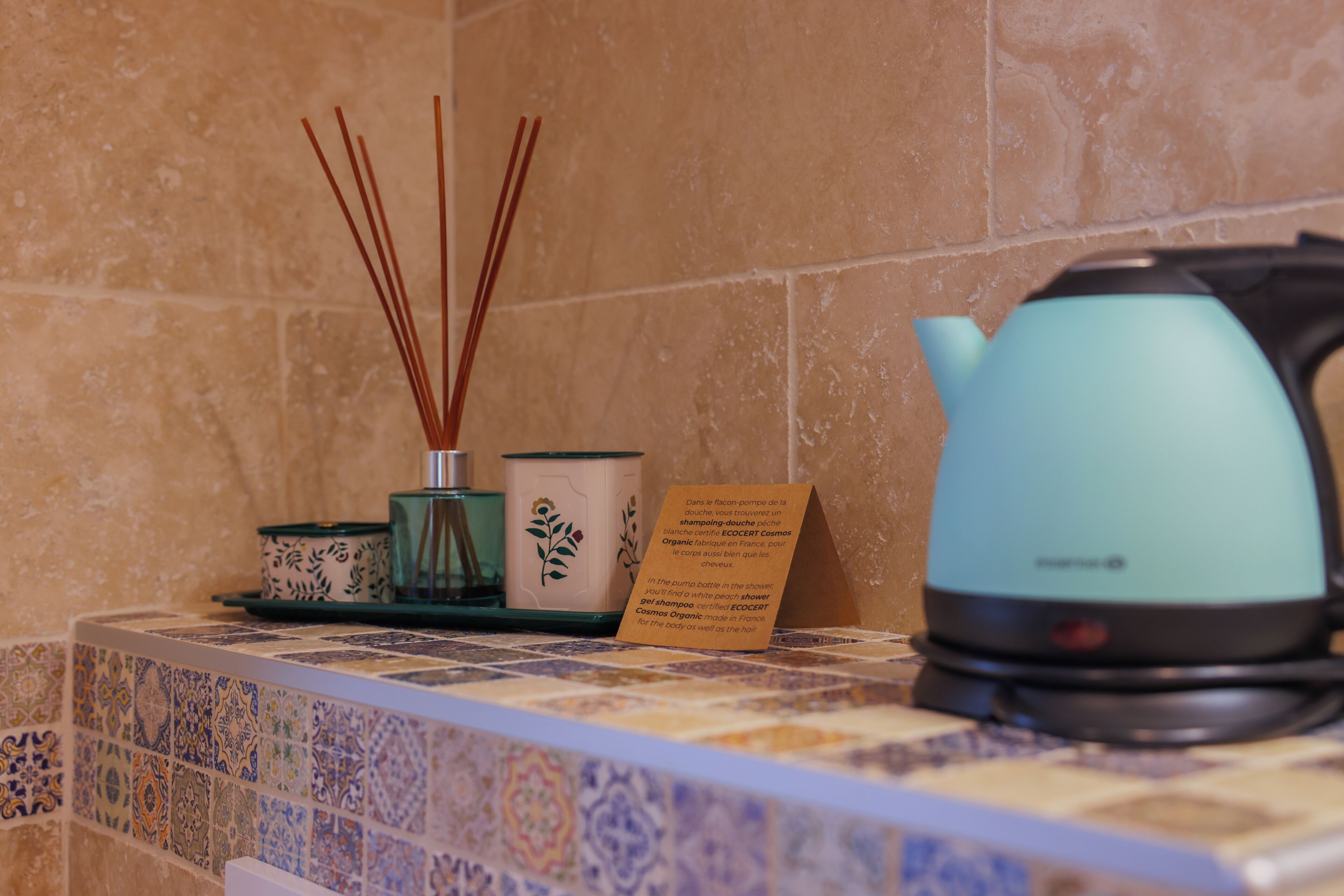 Un baño con pared de azulejos, una tetera color turquesa y una pequeña señal con texto.