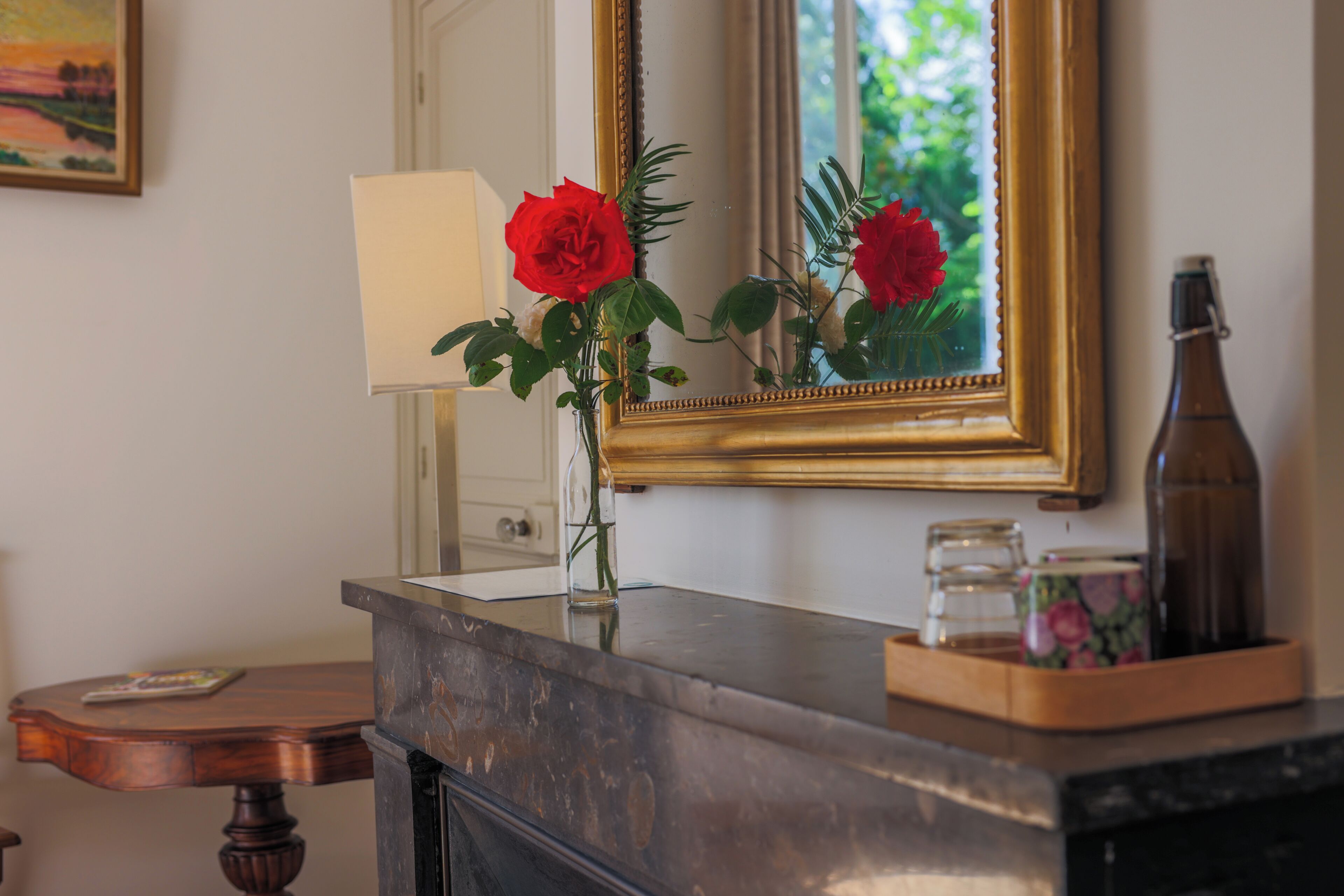 A bathroom vanity with a mirror, a vase with red roses, and a bottle on the counter.
