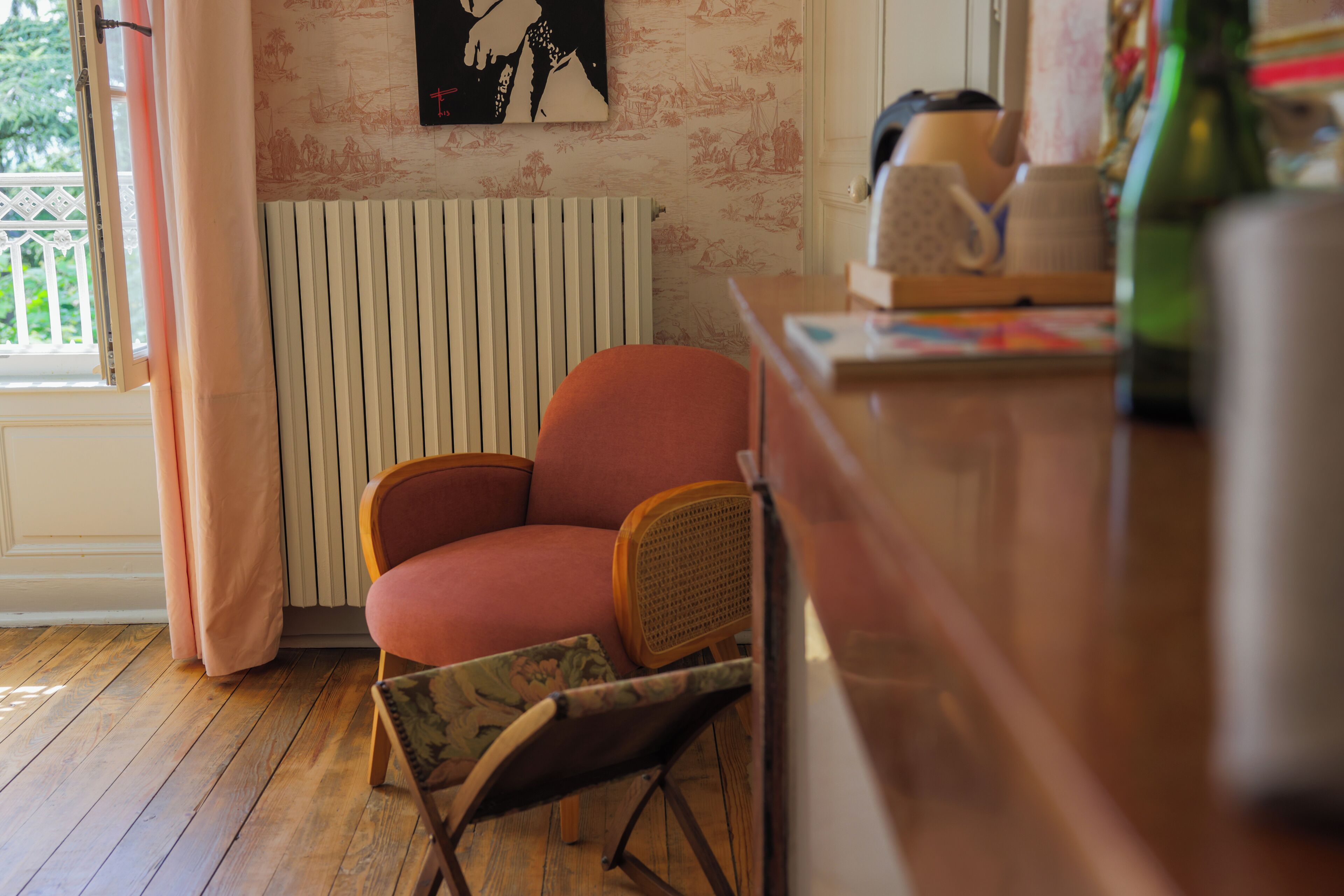 Une pièce avec un plancher en bois, un fauteuil rouge, un radiateur et une fenêtre avec des rideaux.