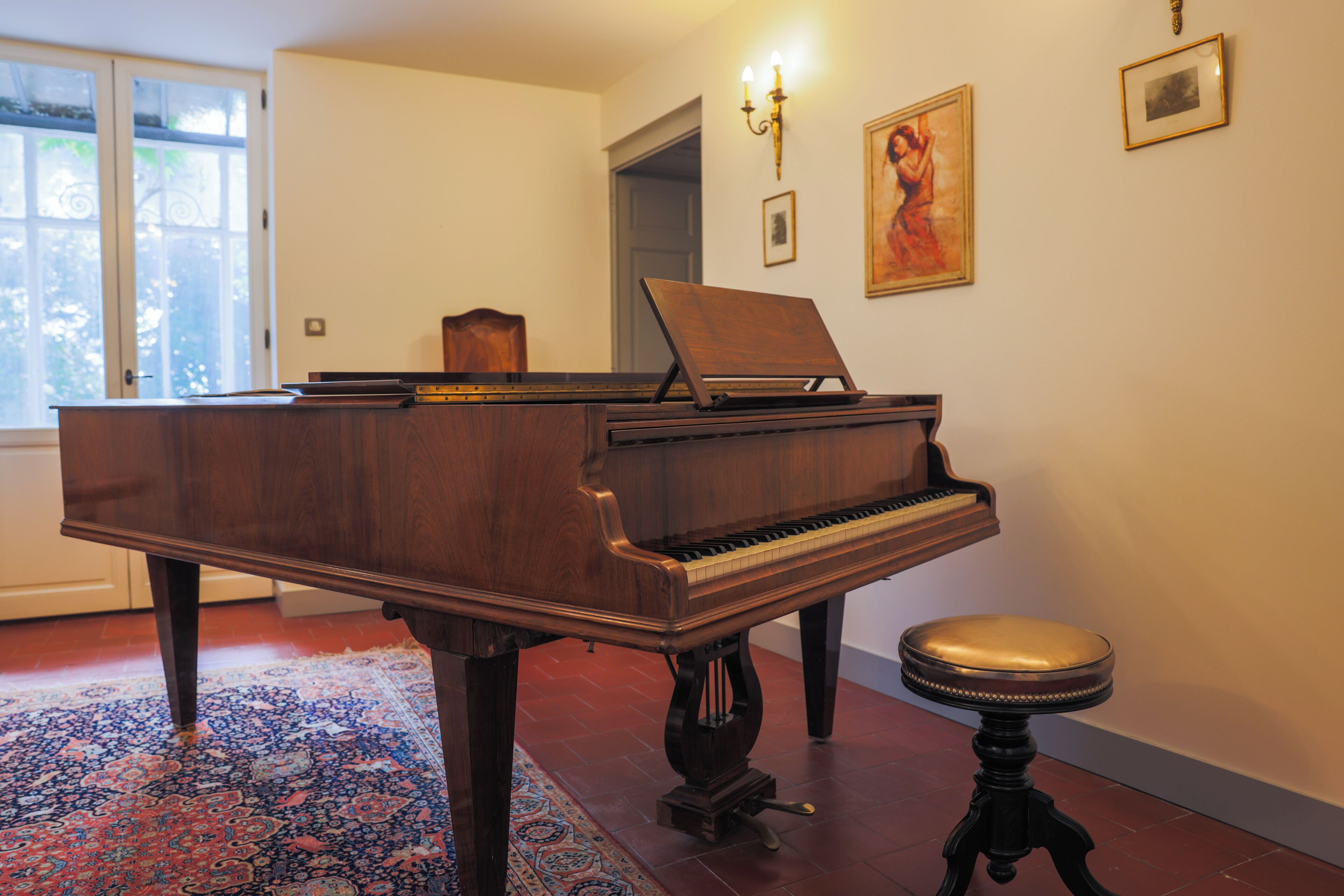 A grand piano in a room with a patterned rug, a stool, and wall-mounted lights.