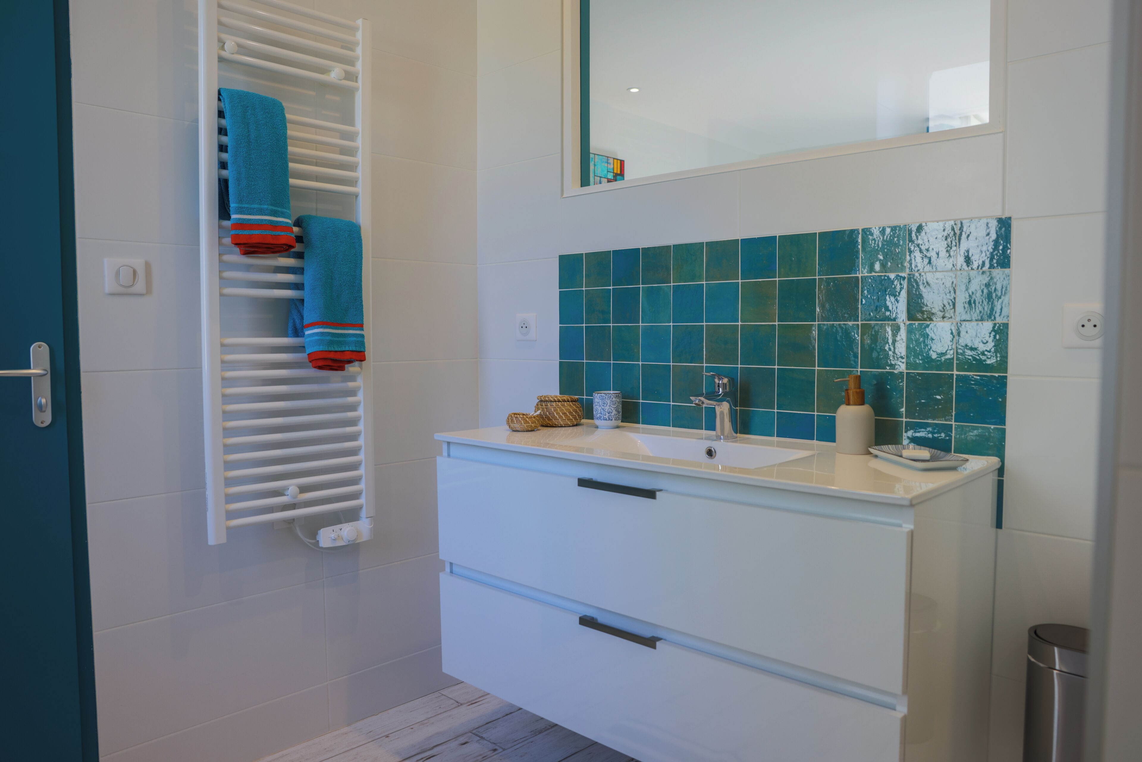 Une salle de bain avec un meuble-lavabo blanc, un miroir et un porte-serviettes avec des serviettes bleues.
