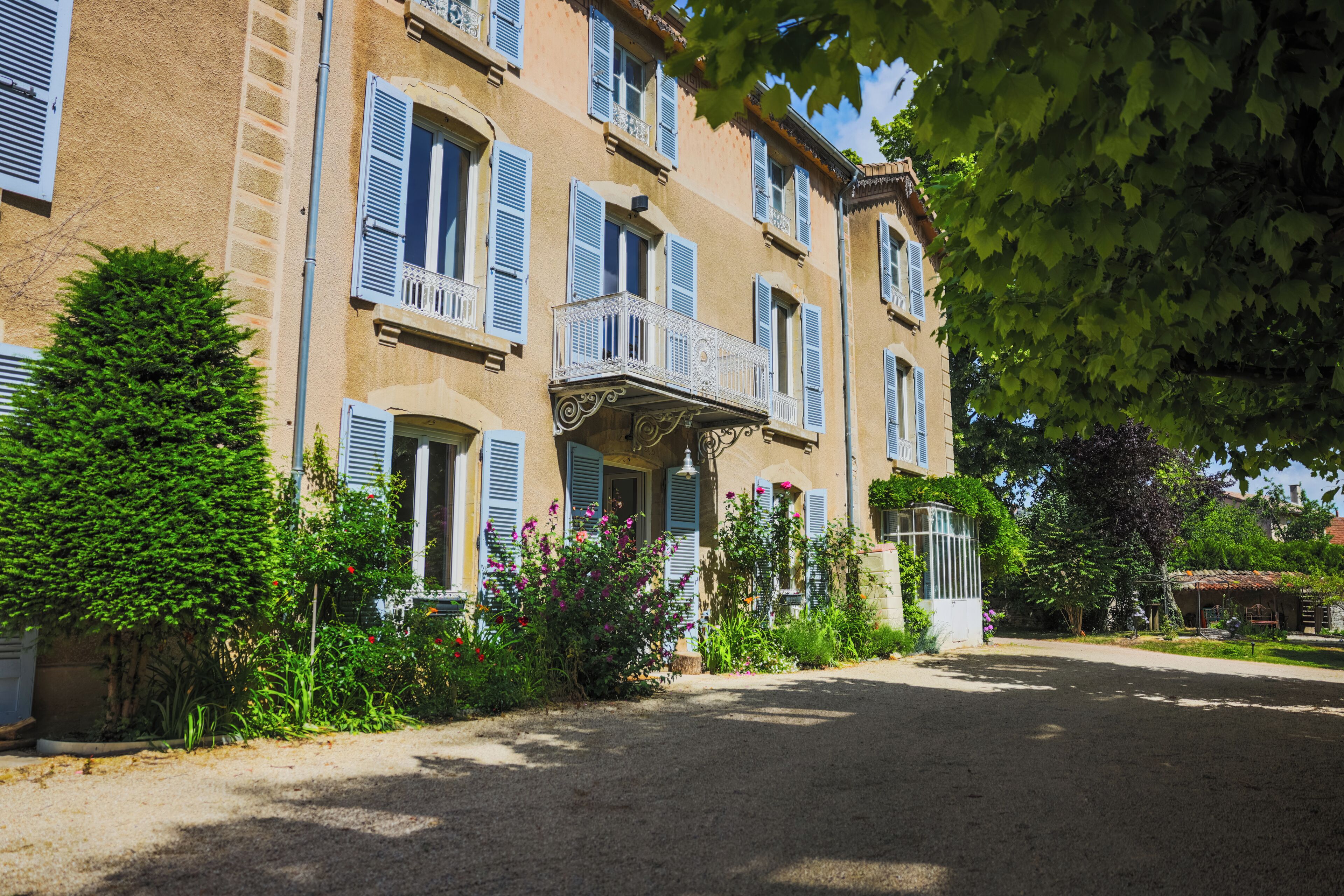 A multi-story building with balconies, a gravel driveway, and surrounding greenery.