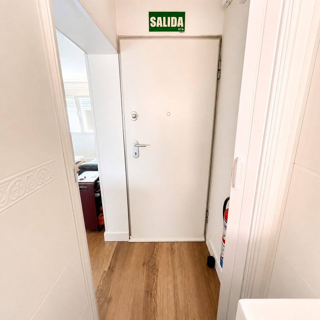 A hallway with a white door marked 'SALIDA' (exit), a wooden floor, and a white wall.