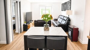 Ein modernes Wohnzimmer mit Esstisch, schwarzer Ledersofa und Fernseher.