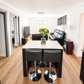 Un salon moderne avec une table à manger, un canapé en cuir noir et un téléviseur.