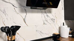 Eine Küche mit einem Flachbildfernseher an der Wand, einem Holzschnittbrett, einer schwarzen Behälter mit Besteck, einer Rolle Küchenpapier und einer kleinen, schwarzen Schachtel mit dem Aufdruck 'SAL'.