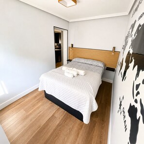 Une chambre moderne avec une tête de lit en bois, un lit recouvert de linge de lit blanc et un mur orné d’un motif abstrait en noir et blanc.