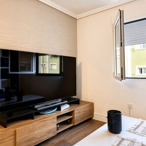 Un soggiorno moderno con una TV a schermo piatto montata su una parete in legno, una finestra con persiane e un tavolo bianco con un tappeto decorativo.