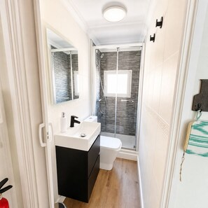 Une petite salle de bain avec un lavabo blanc, un meuble noir et une cabine de douche en verre.