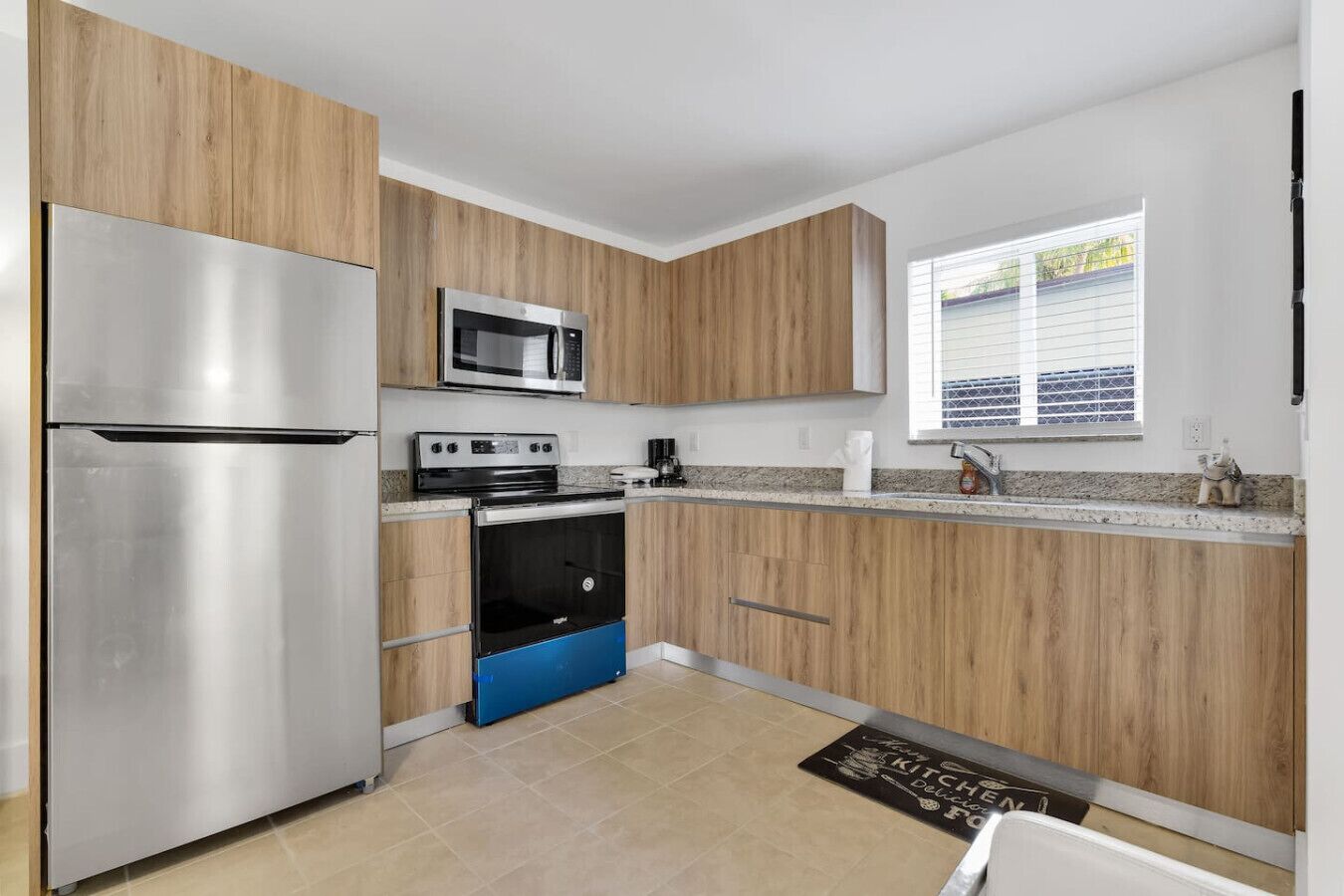 Une cuisine moderne avec des meubles en bois, des appareils électroménagers en acier inoxydable et une fenêtre équipée de stores.