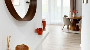 Una sala de estar moderna con una consola blanca, un espejo grande y un comedor con una mesa redonda y sillas.