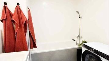 Een compacte badkamer met een wit bad, een wasmachine en een zwarte mat op de vloer.