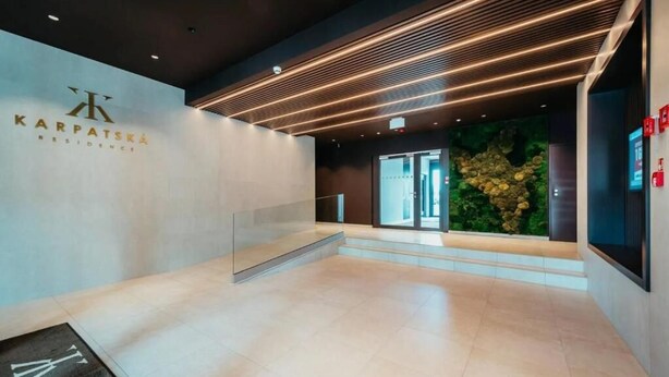 Un moderno vestíbulo de hotel con mostrador de recepción, separador de vidrio y una pared decorativa con diseño de piedra natural.