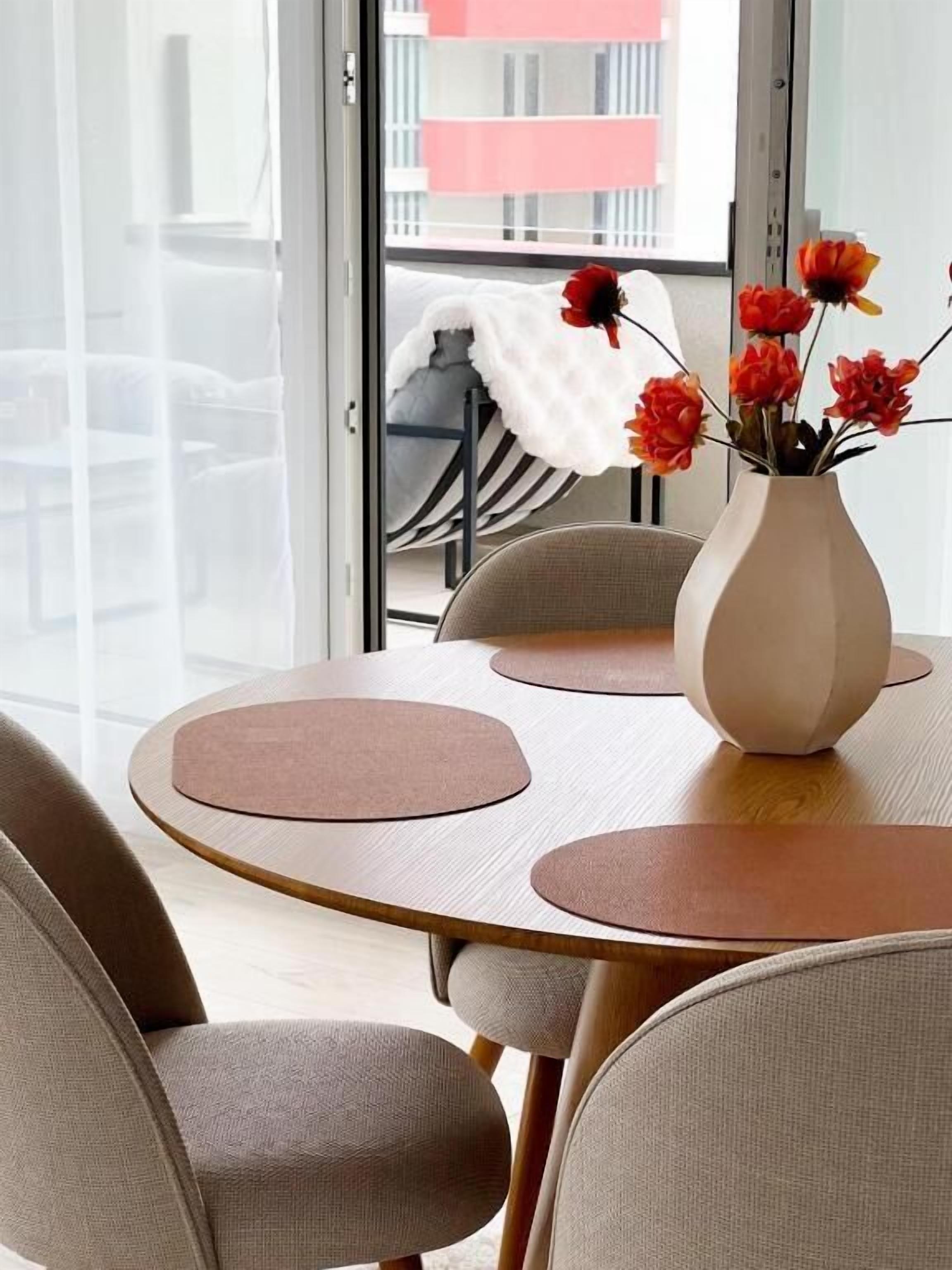 Een moderne eetruimte met een ronde tafel, beigekleurige stoelen en een vaas met rode bloemen.