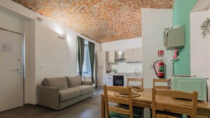 Un salon avec un canapé, une table à manger avec des chaises, un coin cuisine avec des placards, un plafond en briques et un extincteur.