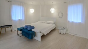 A modern bedroom with a large bed, a small round table, a blue bench, and a glass side table. - 1 bedroom gorgeous apartment in Pieve di Teco (Pieve di Teco)