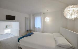 Un dormitorio moderno con una cama grande, una mesita redonda pequeña, un televisor montado en la pared y una lámpara en el techo.