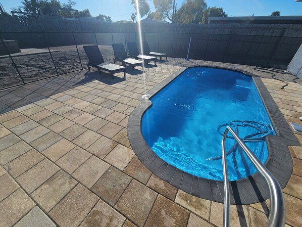 Une piscine dotée d’une terrasse carrelée, de chaises longues et d’une échelle en métal.