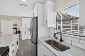 A modern kitchen with white cabinetry, a stainless steel sink, and a window with blinds. - Florida Retreat 3 miles IMG 10 Miles Beach (Bradenton)