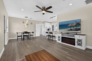 A modern living room with a dining area, kitchen, and a fireplace.