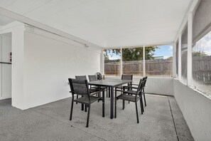 A covered patio with a table and chairs, a fire extinguisher, and a view of a wooden fence.