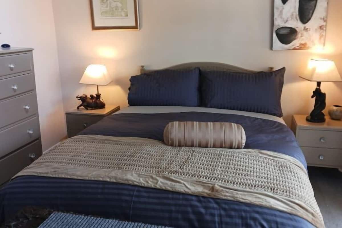 Un lit bien fait, recouvert d’une couvre-lit bleue et beige, avec deux lampes de chevet et un petit objet décoratif sur chaque table de chevet.