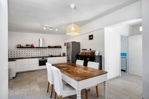 A modern kitchen with white cabinetry, a wooden dining table, and a hanging light fixture.