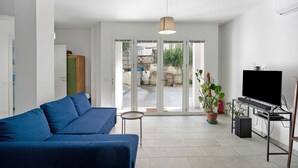 Un salon moderne avec un canapé bleu, un téléviseur posé sur un meuble et une porte-fenêtre coulissante donnant sur un espace extérieur.
