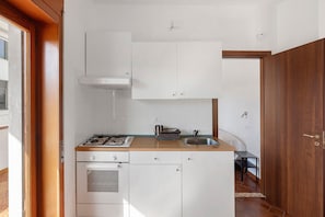 Een compacte keuken met witte kastjes, een gasfornuis, een spoelbak en een klein aanrecht.