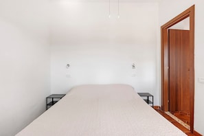 Een slaapkamer met een bed, twee nachtkastjes, een houten garderobe en een witte muur.