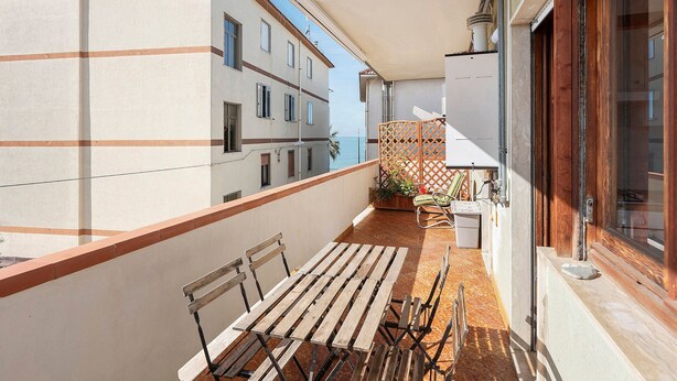 Ein Balkon mit Holztisch und -stühlen, einem Blumentopf und Blick aufs Meer.