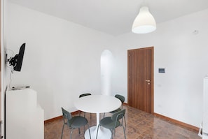 A room with a round table, four chairs, a white ceiling light, a wooden door, and a tiled floor.