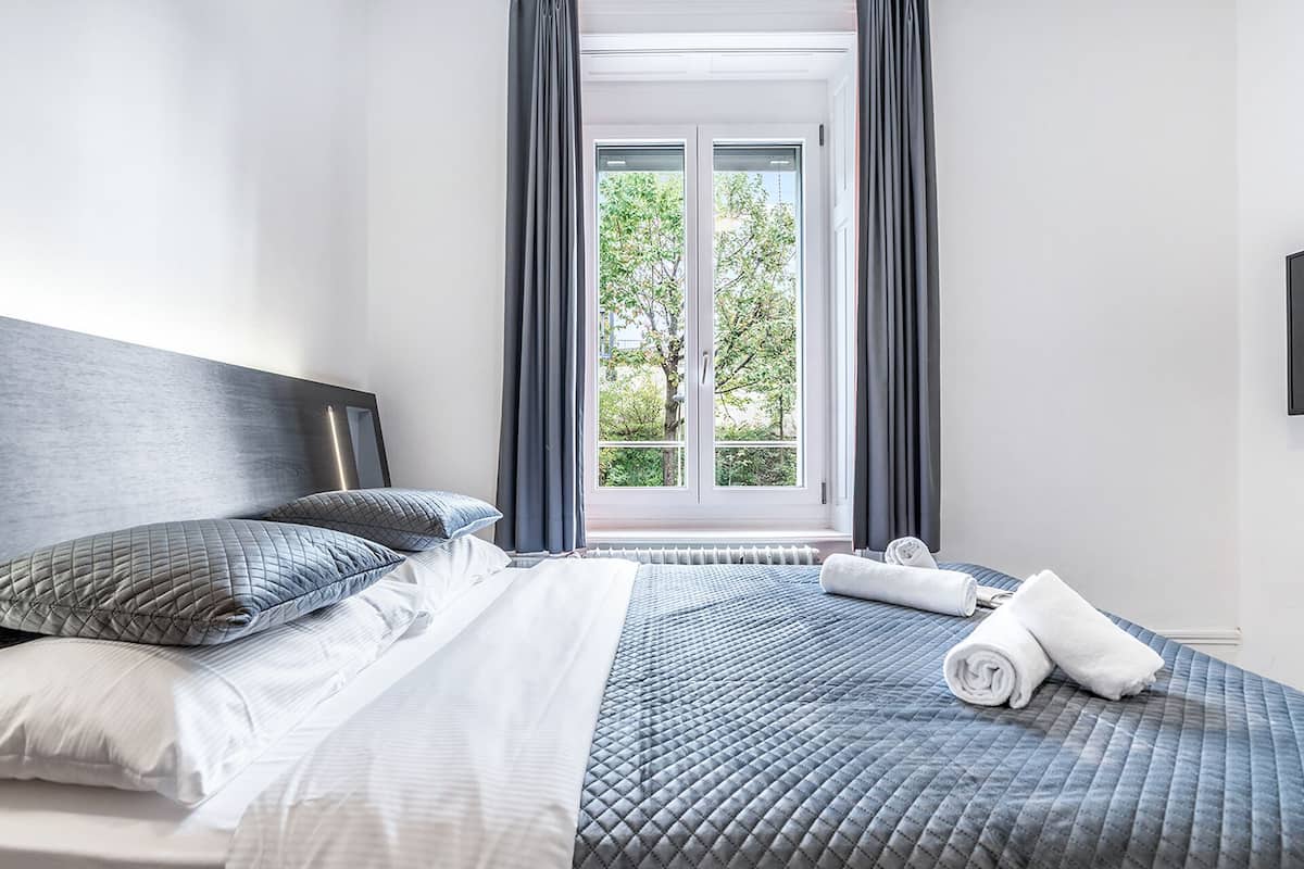 A neatly made bed with a headboard, pillows, and a rolled towel on a bed with a quilted pattern.