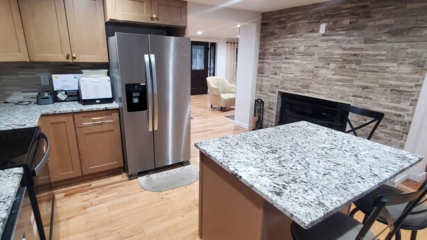 A modern kitchen with wooden cabinets, a stainless steel refrigerator, granite countertops, and a dining area with a table and chairs.