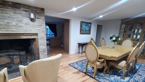 A dining area with a wooden table and chairs, a fireplace, and a stone wall.