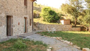 Un edificio in pietra con un vialetto sterrato che conduce a un'area con posti a sedere all'aperto.
