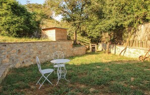 A stone wall with a small wooden structure, two metal chairs, and a table in a grassy outdoor area. - 2 bedroom cozy apartment in Arcidosso (Arcidosso)