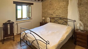 Una camera da letto con una struttura letto in metallo, una finestra con vista, un termosifone e un muro in pietra.