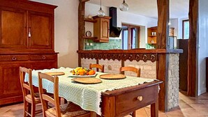 A dining area with a wooden table set for four, surrounded by chairs. A kitchen area is visible in the background with wooden cabinets and a tiled backsplash. - 1 bedroom amazing home in Nanteuil-en-Vallée (Nanteuil-en-Vallée)