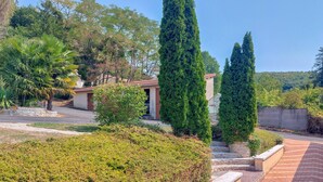 A residential area with a paved driveway, a small building with a red door, and tall evergreen trees. - 1 bedroom amazing home in Nanteuil-en-Vallée (Nanteuil-en-Vallée)
