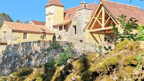 A historic stone building with a prominent tower and a large wooden structure with a steeply pitched roof. - Superbe maison avec piscine (Montgesty)