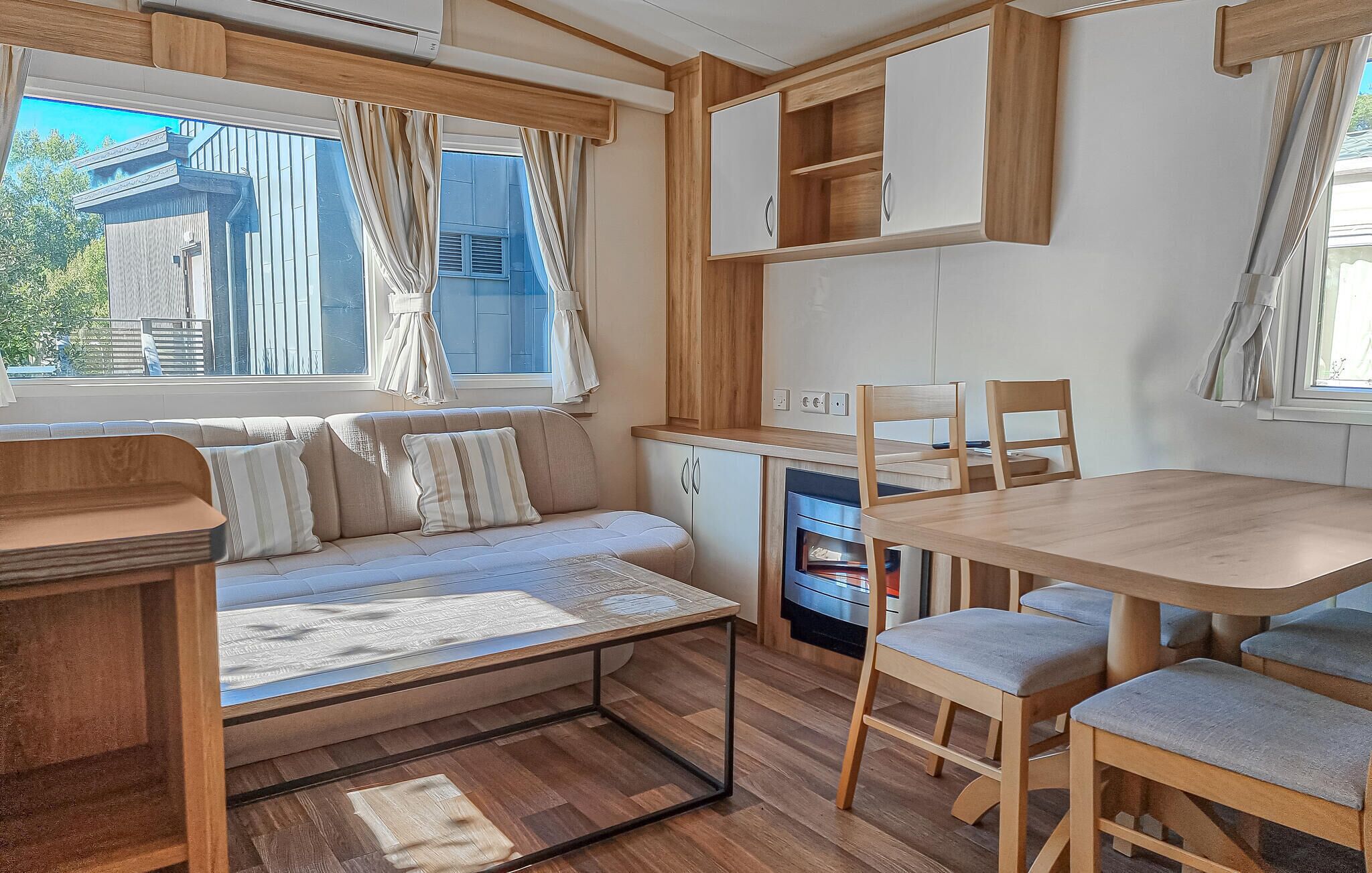 Ett kompakt kök i husbilen med en matplats, inklusive ett träbord och stolar, en inbyggd ugn och en soffa med kuddar.