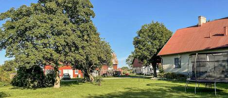 A rural setting with a large tree, a red-roofed barn, and a white building with a screened porch.