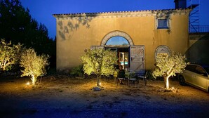 Un edificio con una amplia entrada en arco, un ventanal pequeño y un balcón. Se ven árboles y un coche estacionado al frente.