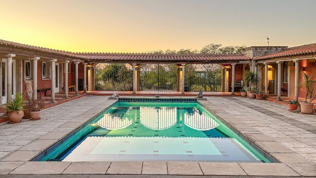 Un área de piscina con suelo de baldosas, rodeada de columnas y plantas en macetas.