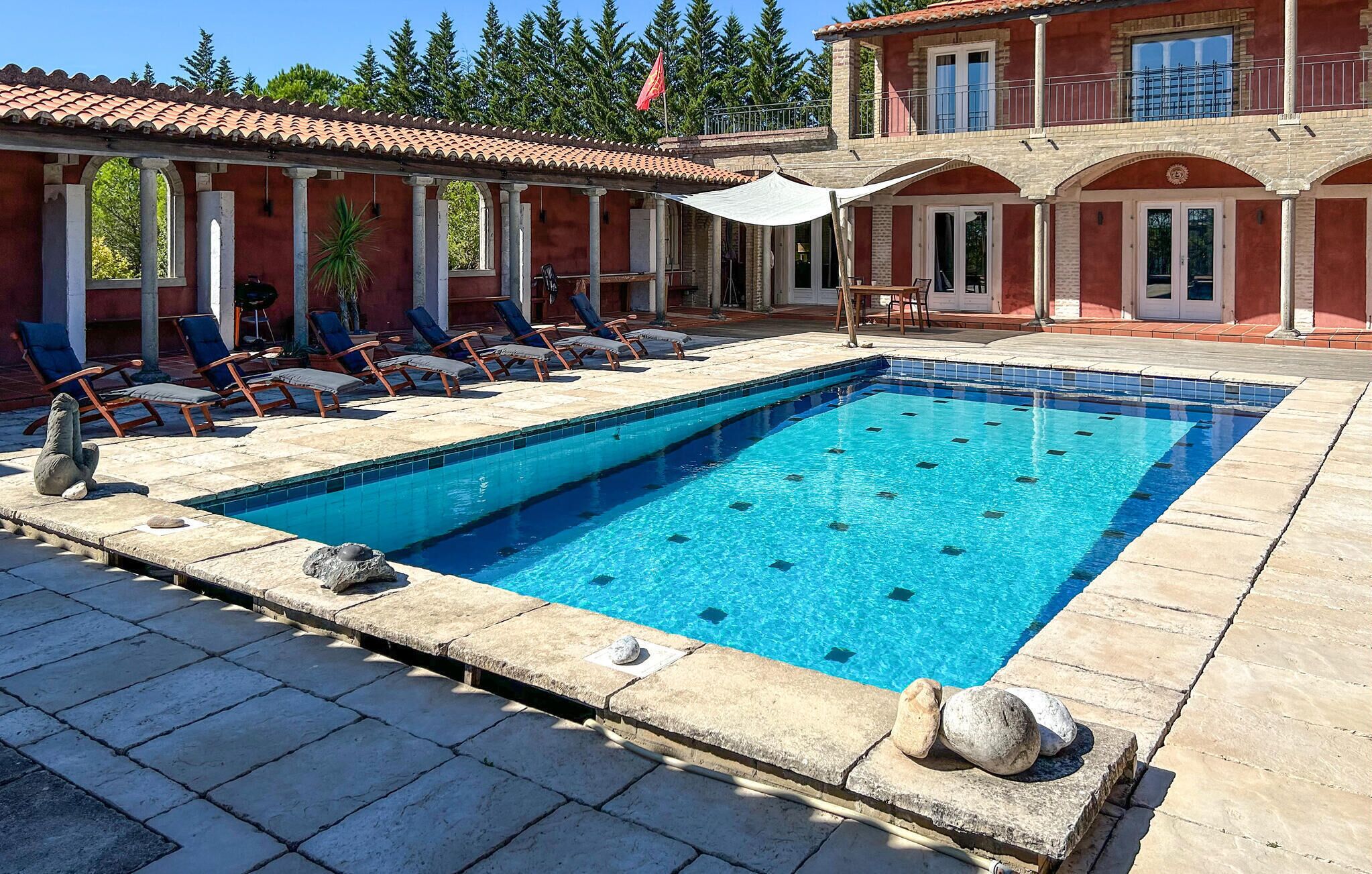 Une piscine rectangulaire à l’eau d’un bleu cristallin, entourée de carreaux de pierre et de chaises longues.