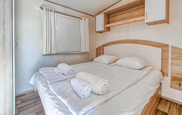 A neatly made bed with white linens and rolled towels, a wooden headboard, and a small wooden cabinet above it.